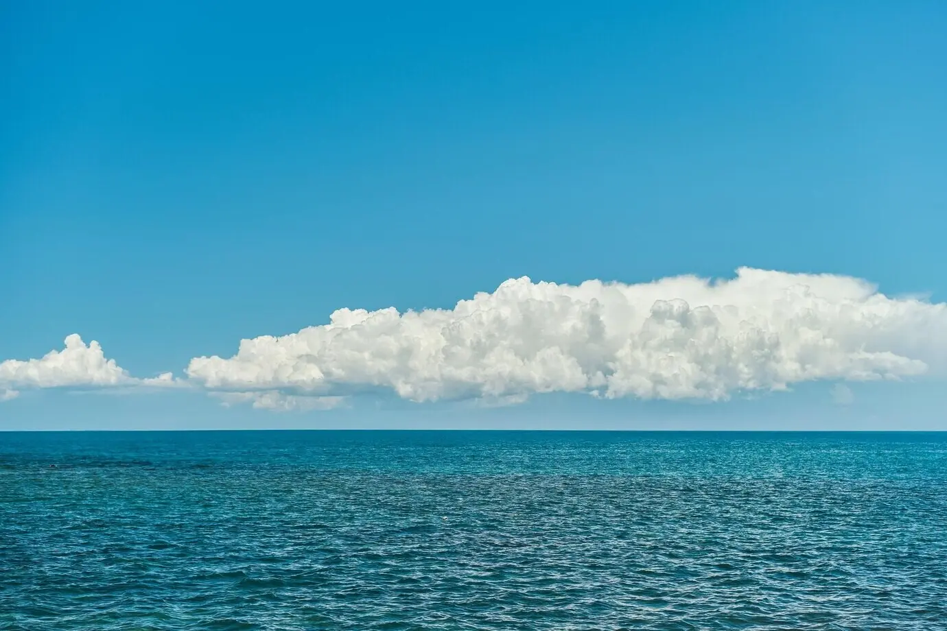 Blick auf ein ruhiges, blaues Meer und Kumuluswolken über dem Horizont; Poster-Konzept zur Bewerbung von Strandurlaub und Inselhopping, mit Freiraum für Seereisen-Werbung.